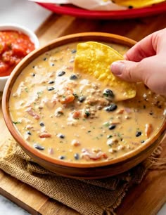 a person dipping a tortilla chip into a bowl of quesadilla soup