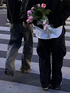 two people walking down the street holding flowers