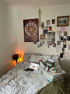 an unmade bed with many pictures on the wall above it and a laptop computer