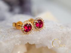 Gold ruby halo earrings, with a delicate yet eye capturing design. The stones have a stunning dark red color that gives you a mesmerizing effect with the accented stones all around. The Ruby is the birthstone of July. It represents love and passion. For centuries, this gem has been considered the king of all gems for its rarity, hardness (second only to a diamond), beauty and apparently mystical powers. Rubies have been the prized possession of emperors and kings throughout the ages, and to this Classic Red Halo Design Earrings, Classic Ruby Earrings With Halo Design, Classic Ruby Halo Earrings, Classic Ruby Halo Design Earrings, Ruby Earrings With Halo Setting In Fine Jewelry, Ruby Halo Earrings In Fine Jewelry Style, Ruby Halo Setting Earrings Fine Jewelry, Ruby Halo Setting Earrings In Fine Jewelry, Ruby Halo Setting Earrings