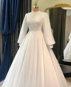 a white wedding dress on display in front of a mirror with blue drapes and curtains