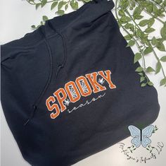 Our Spooky Season Embroidered Hoodie is the perfect way to embrace the Halloween season in style. Its playful design, high-quality applique and embroidery, and comfortable fabric make it a cozy addition to your fall wardrobe. Ready to make a statement this October? Get your hands on our one-of-a-kind hoodie now and show the world you mean business! School Spirit Hoodie For Fall, School Spirit Cotton Hoodie For Fall, School Spirit Hooded Hoodie For Fall, Hooded Sweatshirt With Custom Embroidery For Fall, College School Spirit Hoodie For Fall, Fall Cotton Hoodie With Letter Embroidery, Black Hoodie With Embroidered Graphics For Fall, Trendy Embroidered Logo Hoodie For Fall, College Hoodie With Embroidered Text For Fall