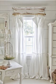 a room with white furniture and curtains on the window sill, in front of a dresser