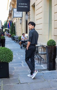 a young man standing on the sidewalk in front of a restaurant with tables and chairs