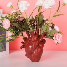 a vase filled with flowers next to a photo frame on a pink background and an image of a human heart