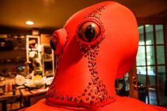 a red sculpture with an eye on it's head and some other things in the background