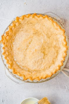 a pie sitting on top of a table next to a bowl of milk and a brush