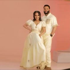 a man and woman dressed in white standing next to each other on a pink background