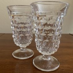 two clear glass goblets sitting on top of a wooden table next to each other