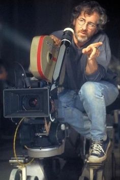 a man sitting on top of a camera in front of a projector with his hand pointing at the camera