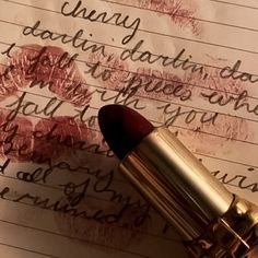 a close up of a lipstick on top of a piece of paper with writing in the background