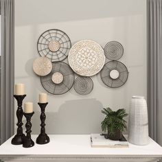 a white table topped with candles next to a vase and wall art on the wall