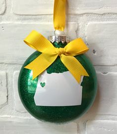 a green ornament with a yellow ribbon hanging on a white brick wall,