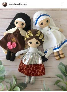 three dolls are sitting next to each other on a wooden surface with plants and greenery