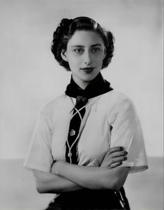 an old black and white photo of a woman wearing a shirt and tie with her arms crossed