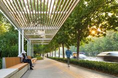 two people are sitting on a bench under a pergolated roof in the park