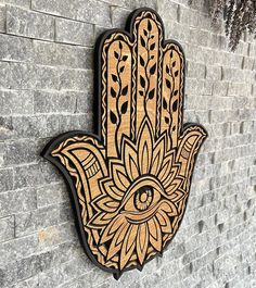 a wooden hamsa hanging on the side of a brick wall with an eye in it