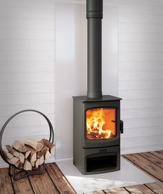 a wood burning stove in a room with white walls and wooden floors, next to a stack of firewood