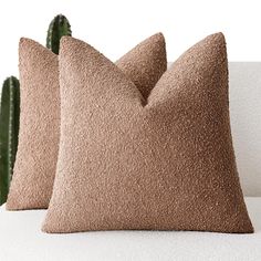 two brown pillows sitting on top of a white couch next to a green cactus plant