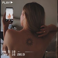 a woman with a sun tattoo on her back taking a selfie in the mirror