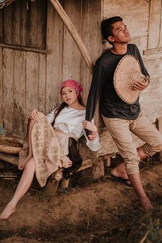 a man and woman sitting on a bench in front of a wooden building holding hats