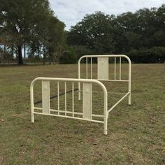 a white metal bed frame sitting in the middle of a field