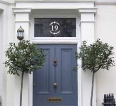 a blue front door with two trees and a house number sign on the top window