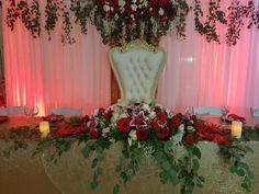 a fancy chair decorated with flowers and greenery on a table in front of pink drapes