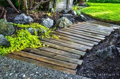 a walkway made out of wooden planks in the middle of a garden with rocks and plants