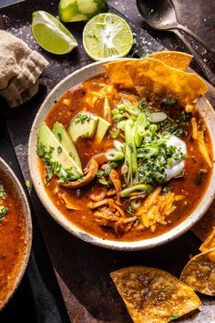 two bowls of soup with tortilla chips and avocado on the side