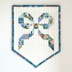 a quilted wall hanging on the side of a white wall with blue and orange flowers