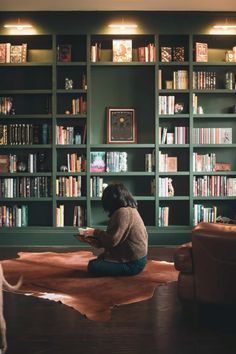 a woman sitting on the floor in front of a bookshelf filled with books