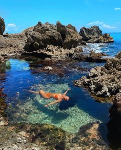 a person swimming in the ocean near some rocks and clear blue water on a sunny day