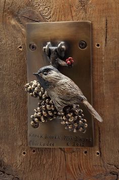 a metal plaque with a bird and berries on it's side, mounted to a wooden wall