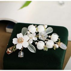 a white flower and leaf brooch on a green velvet box with a book in the background