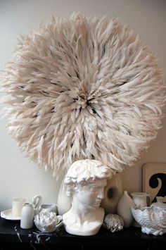 there is a white sculpture with feathers on top of it next to candles and vases