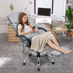 a woman is sitting in an office chair and looking at her cell phone while she relaxes