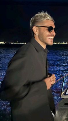 a man in black jacket and sunglasses on boat at night with city lights behind him