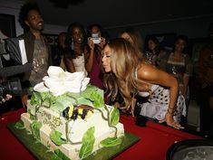 a group of people standing around a table with a cake on it and one woman taking a photo