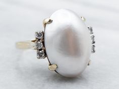 This classic ring is filled with shades of indigo, soft grey, and white! This is a half mabe pearl, shining bright and filled with luster. Framing the pearl is a trio of diamonds, bringing glitter and light into this dreamy vintage piece. Metal: 14K Yellow and White Gold Gem: Mabe Pearl Gem Measurements: 18.6 x 13.4 mm, Oval Accents: 6 Diamonds totaling .18 Carats, SI in Clarity, G in Color Ring Size: 6.25 To view a video of this piece check out the link below: https://vimeo.com/799609528 SKU #: Pearl Diamond Ring, Pearl Cocktail Ring, White Gold Sapphire Ring, Gold Sapphire Ring, Ring Pearl, Diamond Accent Ring, Gold Diamond Engagement Rings, Pearl And Diamond Ring, Mabe Pearl