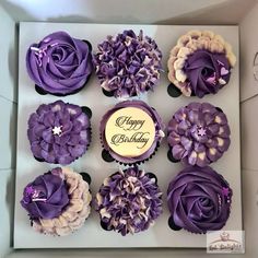 purple cupcakes decorated with flowers in a box