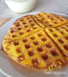 two waffles on a white plate with a bowl of yogurt in the background