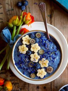 a bowl filled with blueberries and bananas on top of a table next to flowers