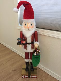 a wooden nutcracker standing next to a window with a santa clause hat on