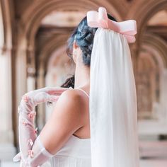 a woman in a wedding dress with a pink bow on her head and veil over her shoulder