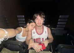 a man sitting next to a woman in a white tank top and black shorts at an event