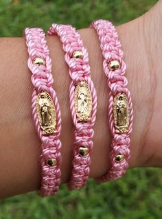 pink and gold braided bracelets with virgin mary on each one side, in front of green grass