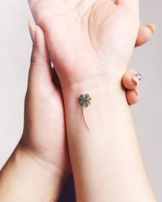 a small four leaf clover tattoo on the left wrist and right hand with a tiny green shamrock