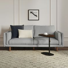 a gray couch sitting on top of a wooden floor next to a table with a coffee cup