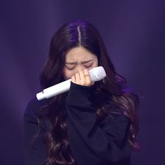 a woman with long dark hair holding a white object to her face while standing in front of a purple background